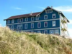 Photograph of the New Cliff House, with three green-painted stories and a peaked roof visible above a grassy bank