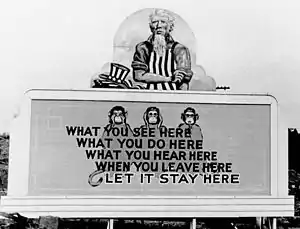 Uncle Sam has removed his hat and is rolling up his sleeves. On the wall in front of him are three monkeys and the slogan: What you see here/ What you do here/ What you hear here/ When you leave here/ Let it stay here.