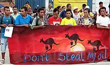 Protestors holding a sign saying "Don't steal my oil" below artwork of kangaroos hopping away with buckets