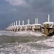 A long row of concrete towers with steel structures connecting them and a very rough sea