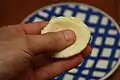 A small piece of dough being flattened in someone's hand