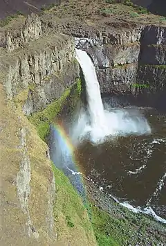 A waterfall surrounded by rocky cliffs with a rainbow visible above the water