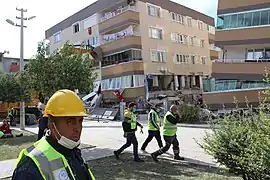 Emergency workers walk past a partially collapsed apartment.