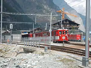 Red-and-white train in front of four-story chalet-style building with gabled roof