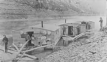 Three Arks for a log drive on Pine Creek, in Lycoming or Tioga County, Pennsylvania. The left ark was for cooking and dining, the middle ark was the sleeping quarters and the right ark was for the horses. The arks were built for just one log drive and then sold for their lumber. The line of the Jersey Shore, Pine Creek and Buffalo Railway can be seen on the eastern shore: the mountainside behind it is nearly bare of trees from clearcutting.