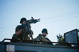 Sharpshooter, with weapon trained, atop a SWAT vehicle