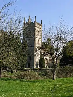 Stone building with prominent square tower. Surrounded by trees and with green grass area in the foreground separated from the building by a stone wall.