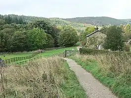 A path leading downhill to a house in a narrow valley, which is surrounded by trees