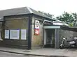 A small, brown-bricked building with a brown-shingled roof and a silver, two-wheeled vehicle sitting idle in front all under a white sky