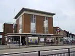 A brown-bricked building with a rectangular, dark blue sign reading "RAYNERS LANE STATION" in white letters all under a dark blue sky