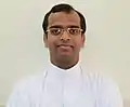 Smiling, bespectacled priest in white tunic