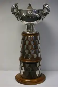 Sterling silver bowl with gold trim and three handles in the shape of leopards atop of a wooden plinth