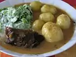 Rolada covered in sauce with potatoes and salad on the side