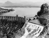 Roosevelt Dam's downstream side, with Lake Roosevelt full, and the spillway on the dam's left embankment is being used to release water.