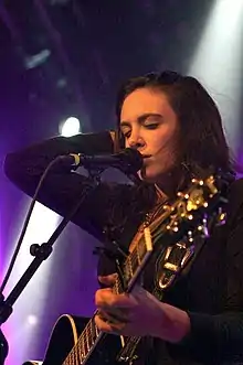 Country singer Rose Falcon, strumming a guitar and singing into a microphone