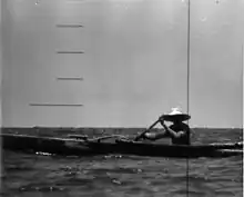 A man wearing a broad straw hat is rowing an outrigger dugout canoe has seen the periscope of the nuclear submarine USS Triton