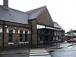 A brown-bricked building with a rectangular, dark blue sign reading "RUISLIP STATION" in white letters all under a clear, white sky