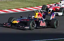 a dark blue F1 car drives along a track ahead of a pink F1 car