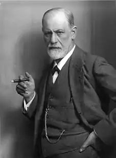 photograph of a balding man with a beard; holding a cigar and wearing a suit