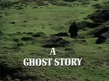 The image is the title screen of the adaptation of "The Signalman". A lone traveller, wearing black Victorian travelling garments and silhouetted so that he cannot be identified, treads across green fields pockmarked by molehills. He is walking towards the camera. A slightly muggy, cloudy atmosphere pervades the image. The strand title "A Ghost Story" is superimposed over this in bold, white capital letters.