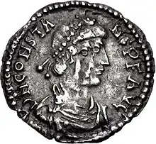 A silver coin showing the profile of a man with two strings of beads in his hair.