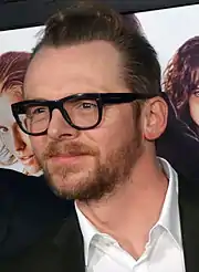 A dark-haired, bearded man wearing glasses and a tieless suit poses for the camera