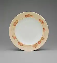 A white shallow bowl with a border of light orange with darker orange flowers and gold streaks.