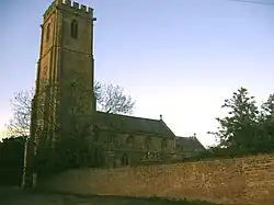 Stone building with square tower, partially obscured by trees.