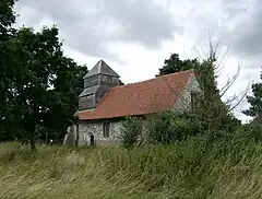 A flint church seen from the southeast, with a red tiled roof and, at the far end, a weatherboarded tower