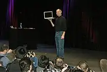 Man in black shirt and jeans holding tablet computer on stage