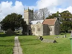 Stone building with square tower. Foreground is grass with gravestones.