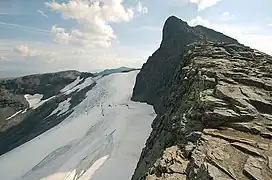 Mountain range composed of dark rock with traces of snow on the sides, against a cloudy blue sky.