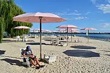 A man sitting under a pink umbrella in an Adirondack chair at Sugar Beach. Several umbrellas and chairs are also visible in the background.