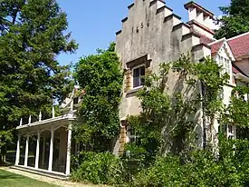 The stepped-gabled west facade of the house, which faces the Hudson River, with the porch – which Irving called his "piazza" – beyond it. It is uncertain why Irving put "1656" at the top of the wall, since the original cottage dates from the 1690s.