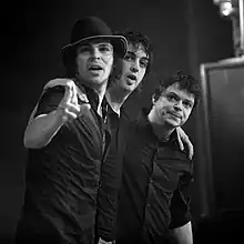 A black-and-white photo of the band embracing and pointing to the camera