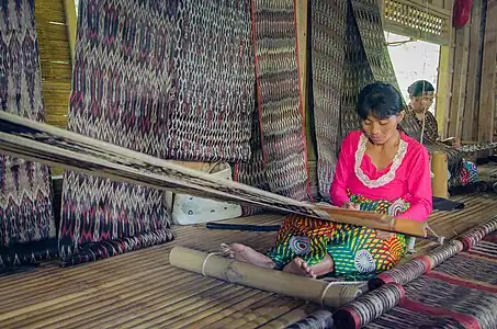 T'boli dream weavers using two-bar bamboo backstrap looms (legogong) to weave t'nalak cloth from abacá fiber. One bar is attached to the ceiling of the traditional T'boli longhouse, while the other is attached to the lower back. Phillipines.