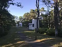 Photo showing the 3 Sisters lighthouses in their new position among the trees and down a winding path away from the coastline. There are 3 similar lighthouses with the beacon in the middle.