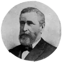 A black and white circular portrait of a Caucasian man in a suit and bow tie