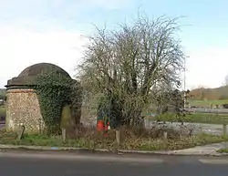 Curious relic from the age of the turnpike. Located at the original junction of the A27 and Ashcombe Hollow, the former has been moved few yards to the north the latter to the right has now been blocked off and a new route takes the lane down to Ashcombe Farm Roundabout. Originally there was a pair but the northern one has been lost to road widening. The existence of fireplaces within the structure has led some to believe this was the domestic part of the tollgate, the collection area having been lost over time. A door is on the northern side and there are two windows either side, the roof was originally bricked in a circular fashion but was stolen in the 1940s before East Sussex County Council restored it in the 1950s. The tollgate opened in 1820 and probably went into disuse when the turnpike was wound up in 1871, after that ownership became a little blurred and was claimed by Sussex Heritage Society in 1996 and has never been contested.