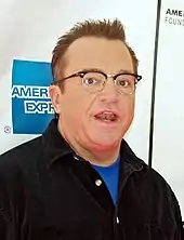 Head shot of an astonished man with glasses wearing a black, unbuttoned shirt.