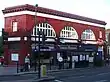 A red-bricked building with a rectangular, dark blue sign reading "TUFNELL PARK STATION" in white letters all under a blue sky with white clouds