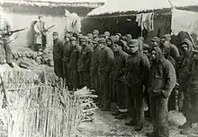 A group of men under guard standing in front of a camera