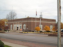 A one-story brick building, seen from its right, with rounded windows and an American flag out front.