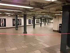 View of a corridor sloping upward from the IRT mezzanine to the BMT mezzanine. The corridor is wide and contains tiled floors, a low ceiling, and green columns.