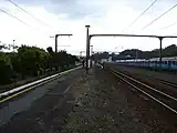 Looking north along the Upper Hutt railway station platform. To the left is the dock and to the right are the main line and crossing loop. Behind the fence (right) is the EMU storage area. In the background is the station building (centre), and neighbouring big-format retailers (right).