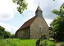 A small stone church with a red tiled roof and a wooden bellcote