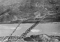 A river with two bridges extending over it, and a large hill on the south bank