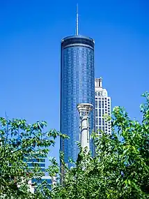 A blue glass cylindrical building topped with a spire