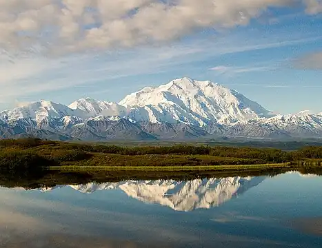 A snow-covered, gently sloping mountain is in the background, with a lake in the foreground