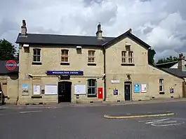 A beige-bricked building with a rectangular, dark blue sign reading "WOODSIDE PARK STATION" in white letters all under a blue sky